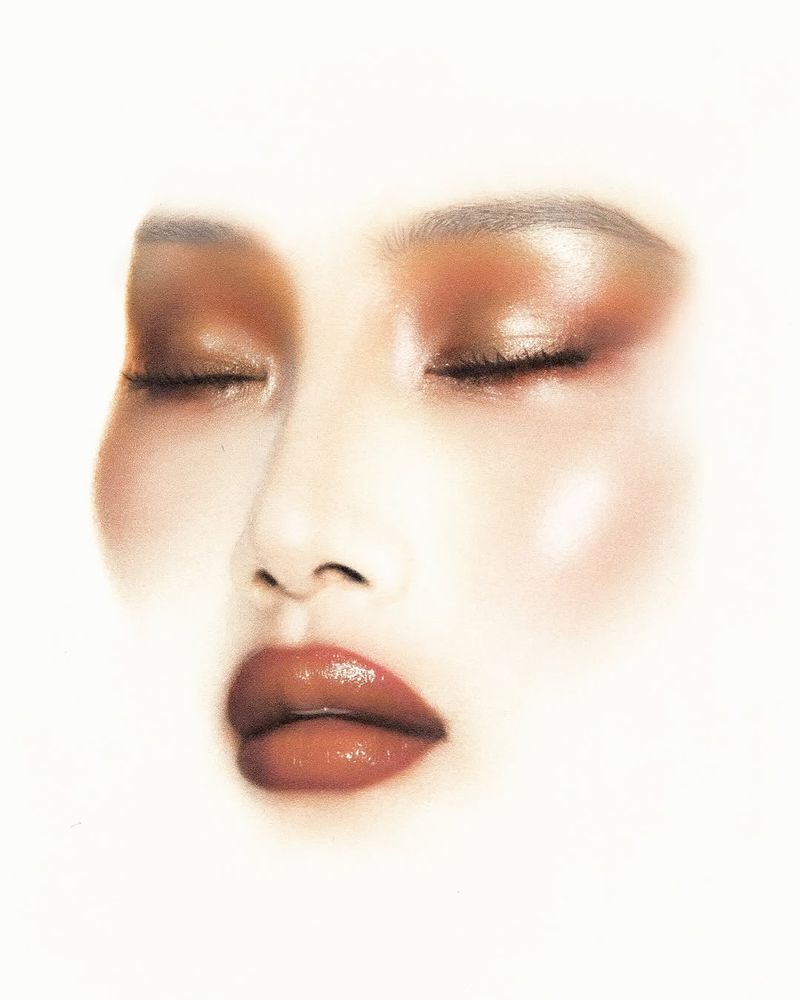 Close-up portrait of a person with closed eyes and glossy lips against a white background, emphasizing the makeup and soft lighting.