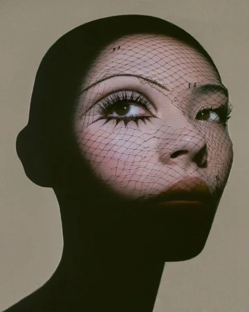 Close-up portrait of a model wearing a black head covering and a fine mesh veil across her face, with dramatic graphic eyeliner.