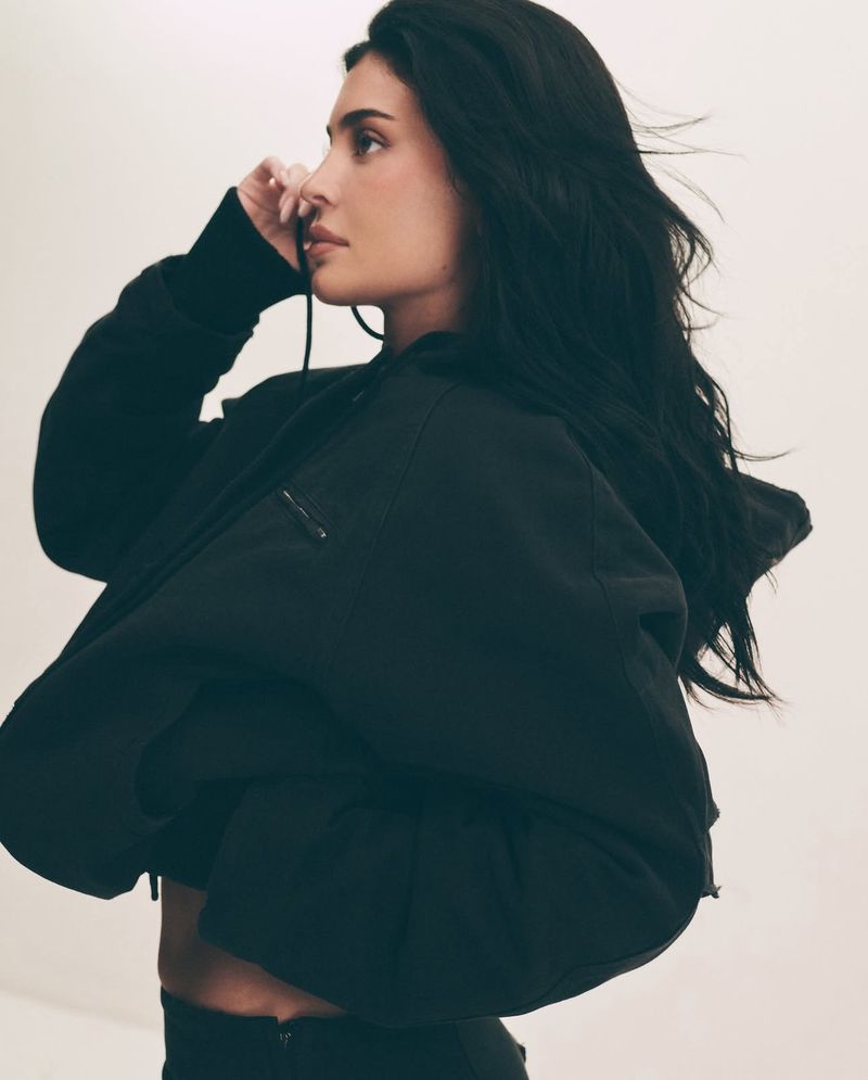 Kylie Jenner wearing a dark zip-up hoodie against a plain white studio background