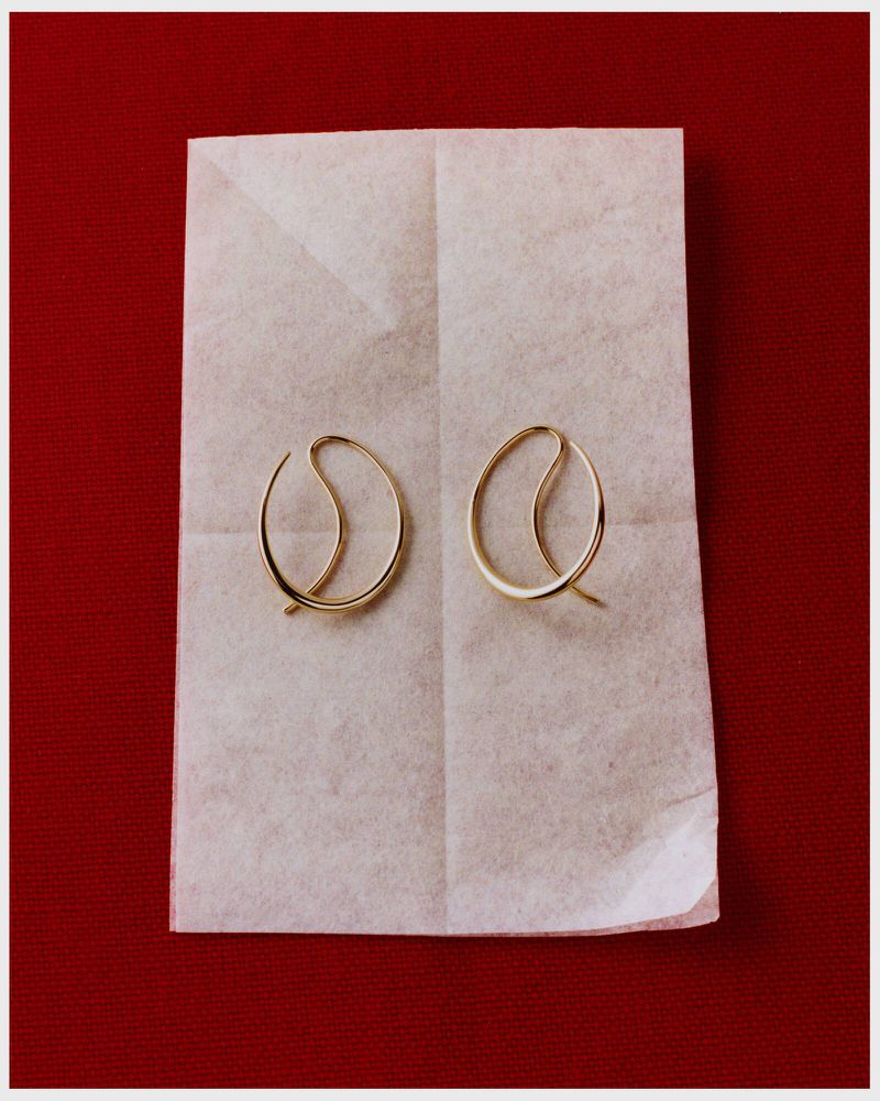 Overhead shot of two gold hoop earrings displayed on a folded piece of parchment paper against a solid red background.