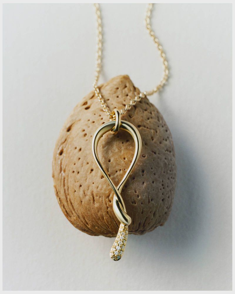 A gold pendant necklace drapes over a textured rock, showcased in a simple studio setting with soft, diffused lighting.