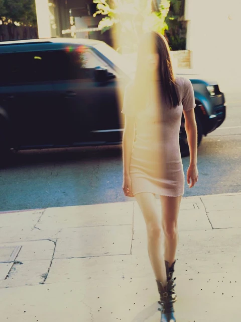 Woman in mini dress walking on the street with a SUV, with natural sunlight and long shadows, in an outdoor urban setting.