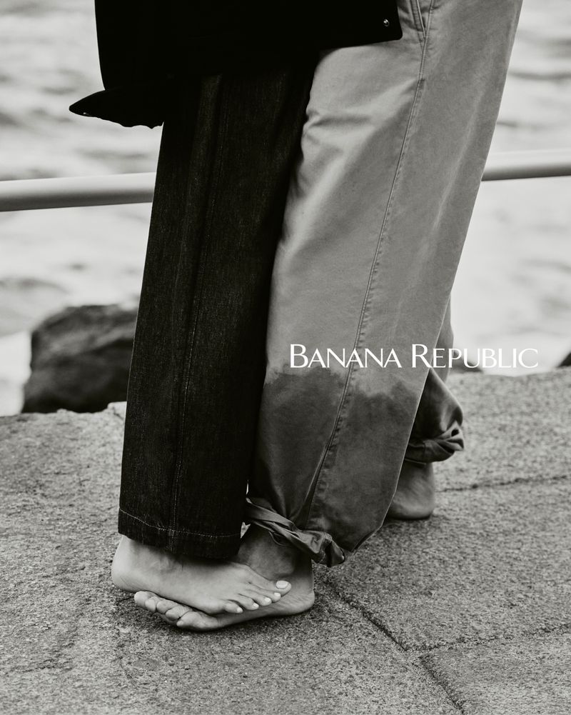 Close-up of two people barefoot on concrete next to water, one in dark jeans, one in light pants, with Banana Republic logo.