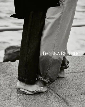 Close-up of two people barefoot on concrete next to water, one in dark jeans, one in light pants, with Banana Republic logo.