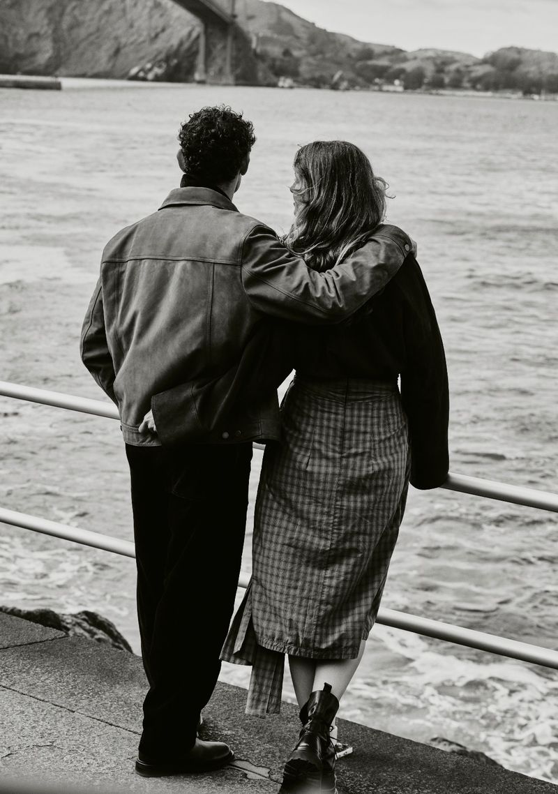 Back view of a couple embracing on a pier overlooking the Golden Gate Bridge and San Francisco Bay in a black and white photograph.