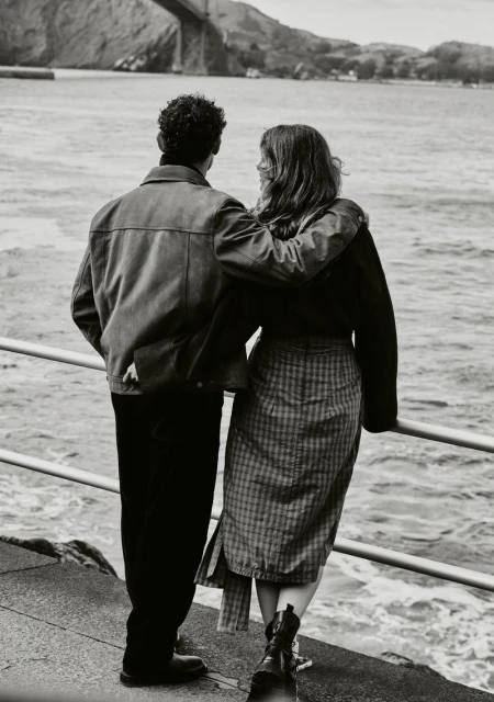 Back view of a couple embracing on a pier overlooking the Golden Gate Bridge and San Francisco Bay in a black and white photograph.
