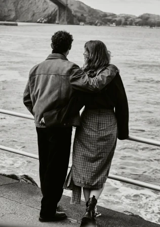 Back view of a couple embracing on a pier overlooking the Golden Gate Bridge and San Francisco Bay in a black and white photograph.