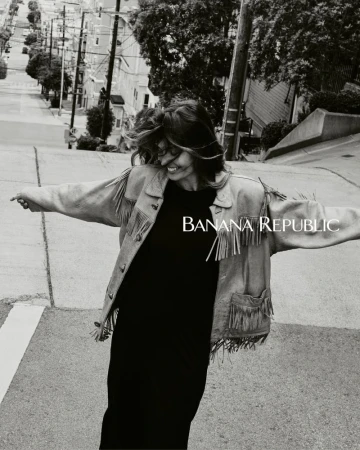 Woman wearing a fringe jacket dances on an angled street in a black and white outdoor shot; Banana Republic logo in the left center.