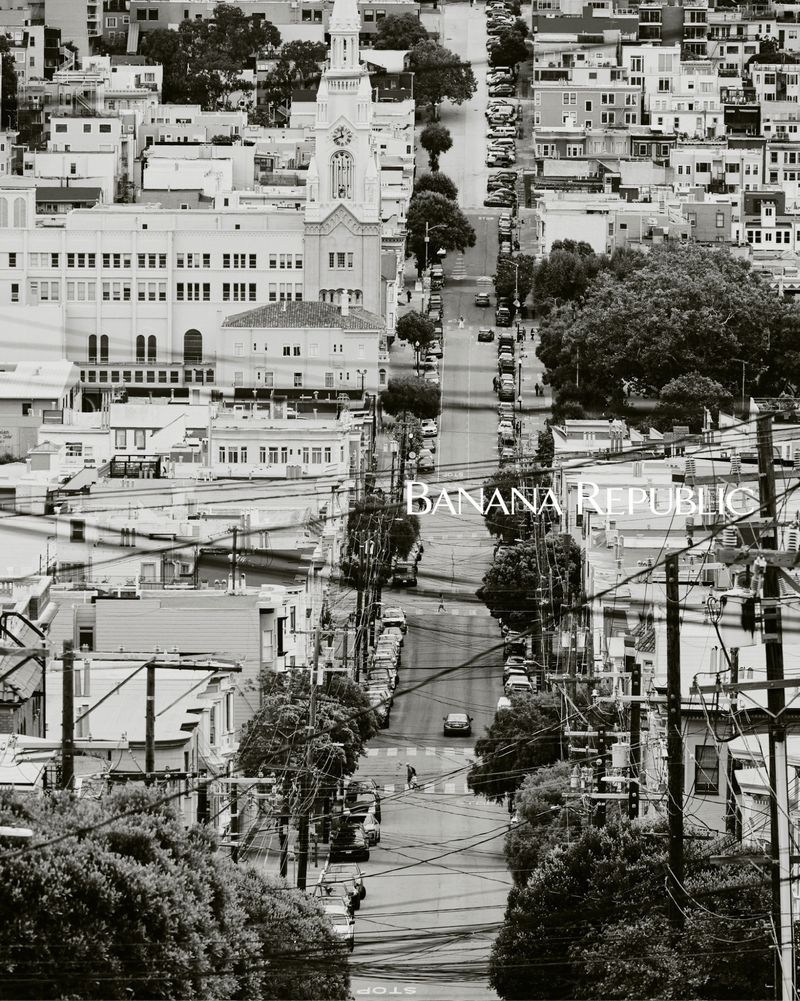 Black-and-white cityscape of San Francisco with a view down a steep street lined with buildings, trees, and cars, featuring the Banana Republic logo.