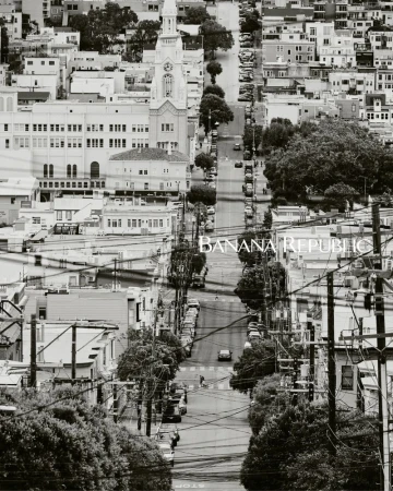 Black-and-white cityscape of San Francisco with a view down a steep street lined with buildings, trees, and cars, featuring the Banana Republic logo.