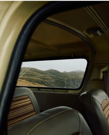 Interior of car with brown seats looking out the back window at a landscape with rolling hills and fog in the distance.