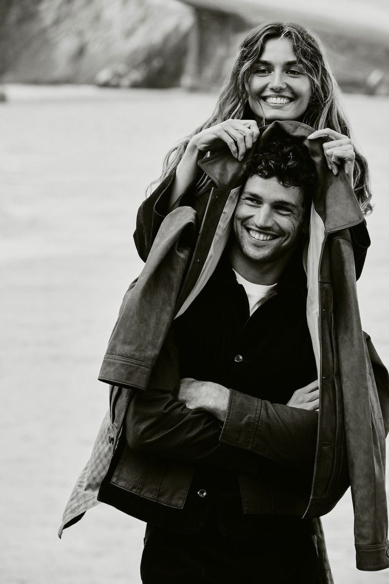 Smiling woman behind a smiling man holding a jacket outdoors in a black and white photograph for Banana Republic