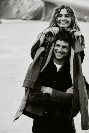 Smiling woman behind a smiling man holding a jacket outdoors in a black and white photograph for Banana Republic