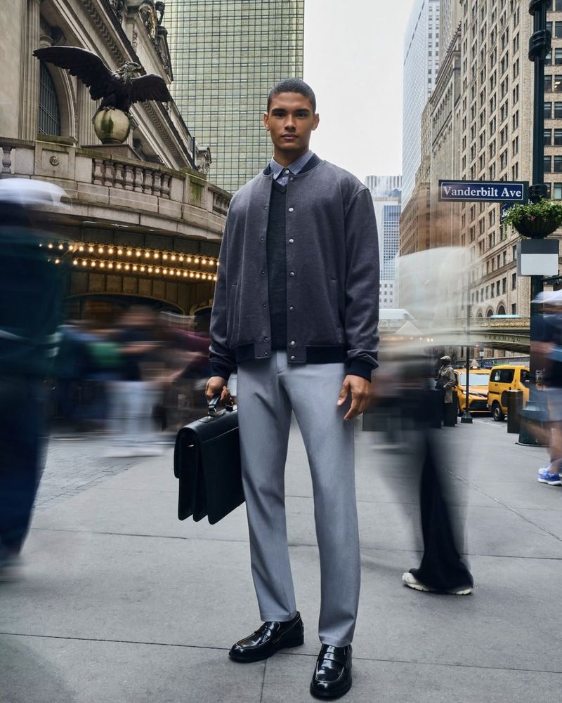 A well-dressed man in an urbane jacket and slacks stands confidently in a bustling city, holding a briefcase amidst blurred pedestrians.