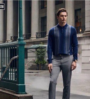 Model Oli Lacey standing on a city street wearing a navy blue patterned knit polo sweater and grey trousers for Van Heusen.