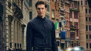 Model Oli Lacey wearing a navy blue dotted long-sleeve dress shirt and black trousers on a city street.
