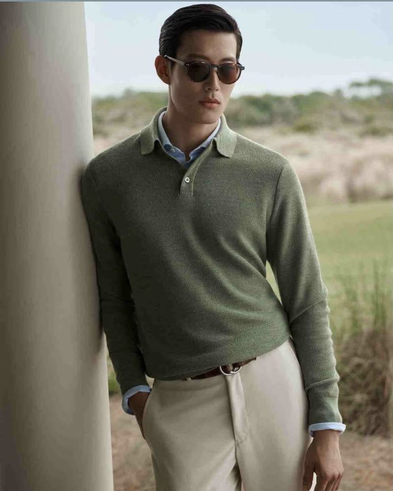 Man wearing sunglasses and a green polo shirt leaning against a concrete pillar outdoors