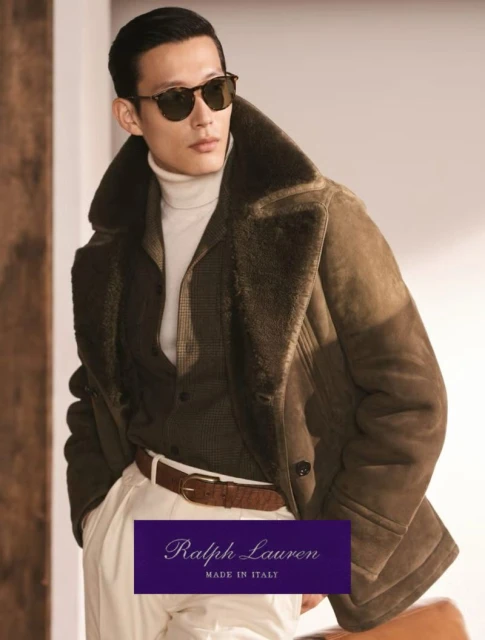 A fashionable Asian man in sunglasses poses wearing a brown shearling coat, white turtleneck, and white pants for Ralph Lauren ad.