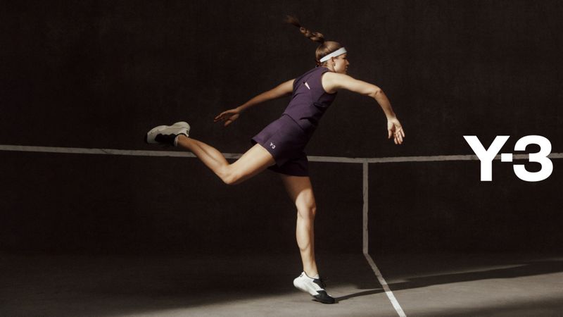 Athletic woman in purple activewear strikes a dynamic pose on a grey court with Y-3 logo, showcasing fitness and fashion.