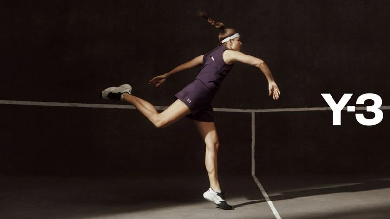 Athletic woman in purple activewear strikes a dynamic pose on a grey court with Y-3 logo, showcasing fitness and fashion.