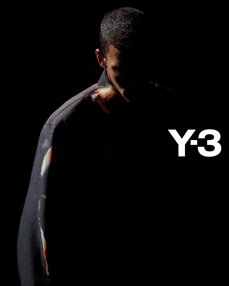 Dark, moody fashion shot featuring a man wearing a jacket, posed against a black background, highlighting the clothing and Y-3 logo.