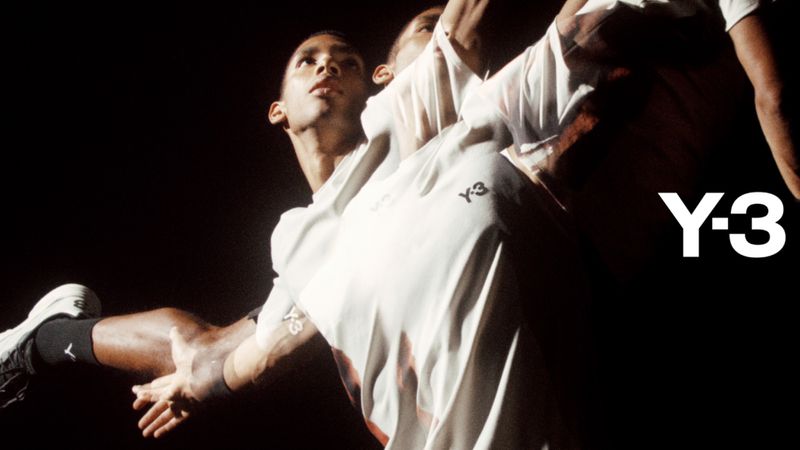 Two Black male adults in motion, illuminated against a dark background, wearing white t-shirts and black and white athletic shoes; Y-3 brand logo.