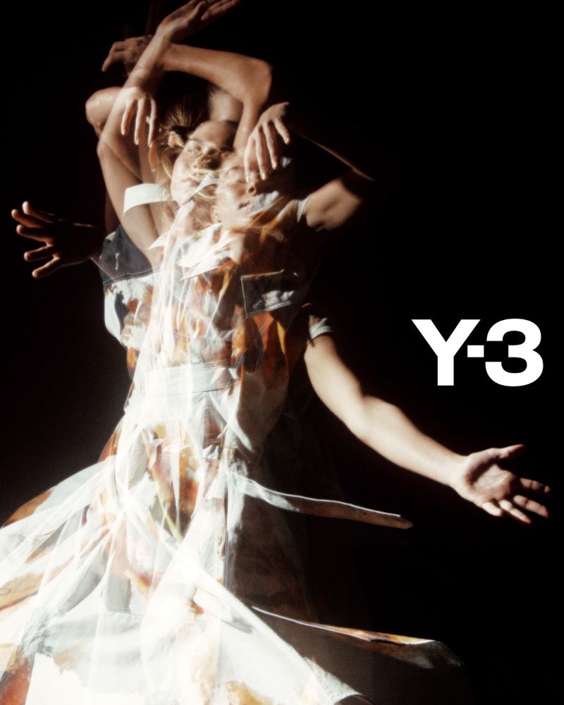 Woman wearing printed white dress poses dynamically in a studio with blurred motion effect, highlighted against a stark black backdrop.