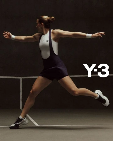 A woman wearing a white and navy athletic bodysuit and athletic shoes is in motion on an indoor court with a dark background.