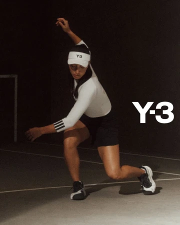 A woman wearing athleisure apparel swings a tennis racket. She is wearing a hat, long sleeve shirt, and a tennis skirt against a dark backdrop.