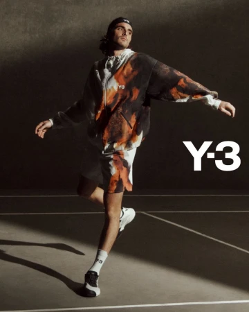 A man in a Y-3 printed hoodie and shorts poses dynamically on a neutral court with directional lighting, showcasing modern fashion.