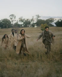 Five models wearing winter coats running through a grassy field under an overcast sky for The Woolmark Company
