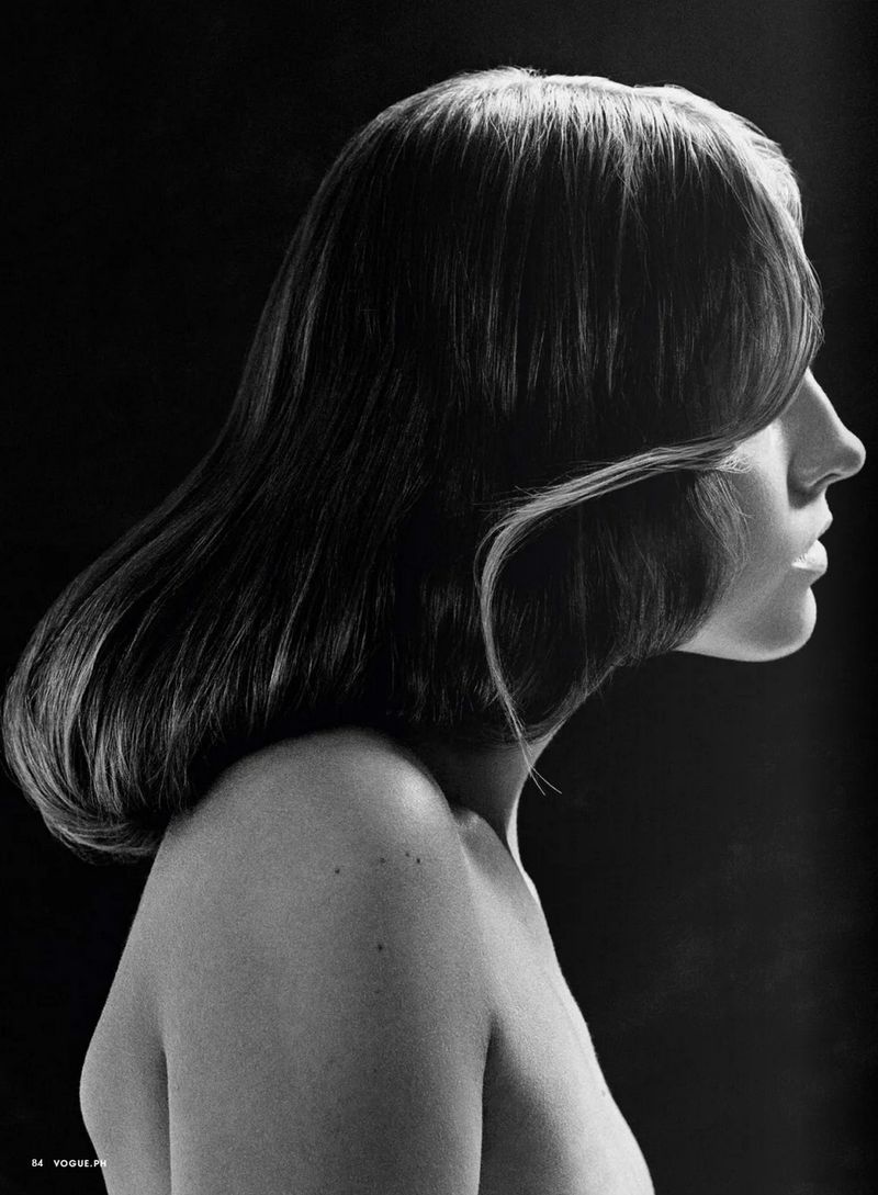 Monochrome portrait of a topless adult female with shoulder-length hair and clean skin tone against a black background.
