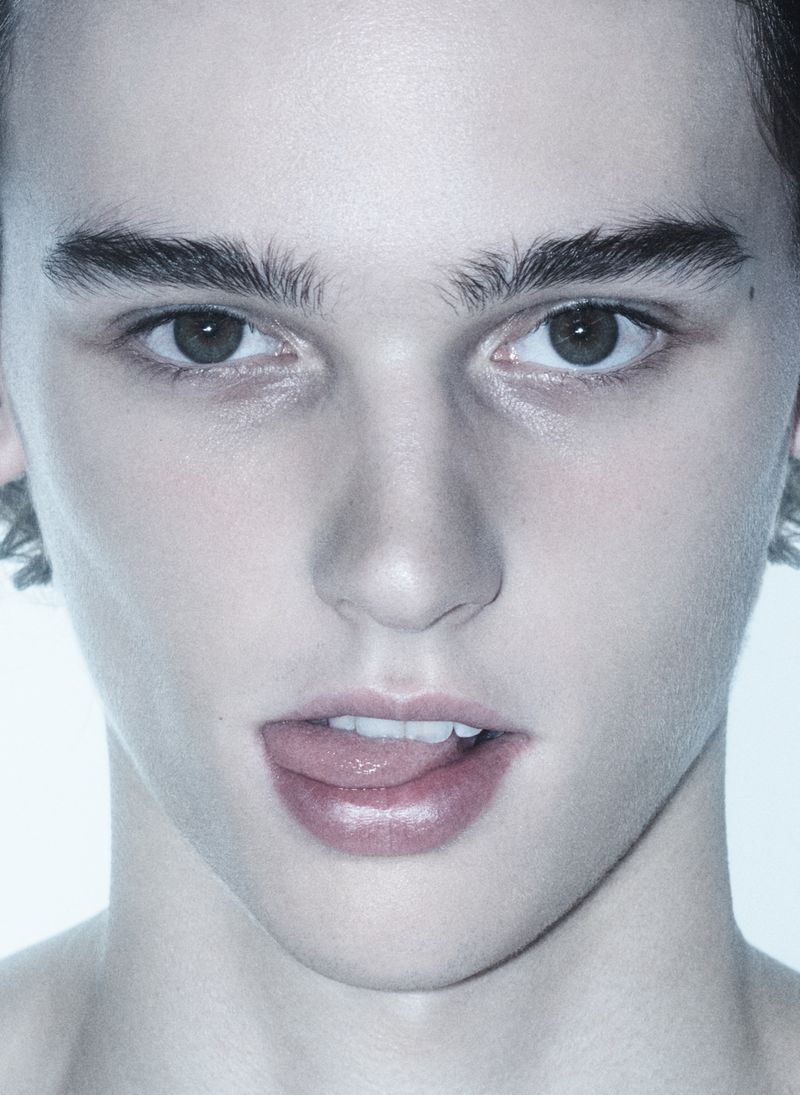 Extreme close up portrait of a young male model sticking out his tongue against a bright white background.
