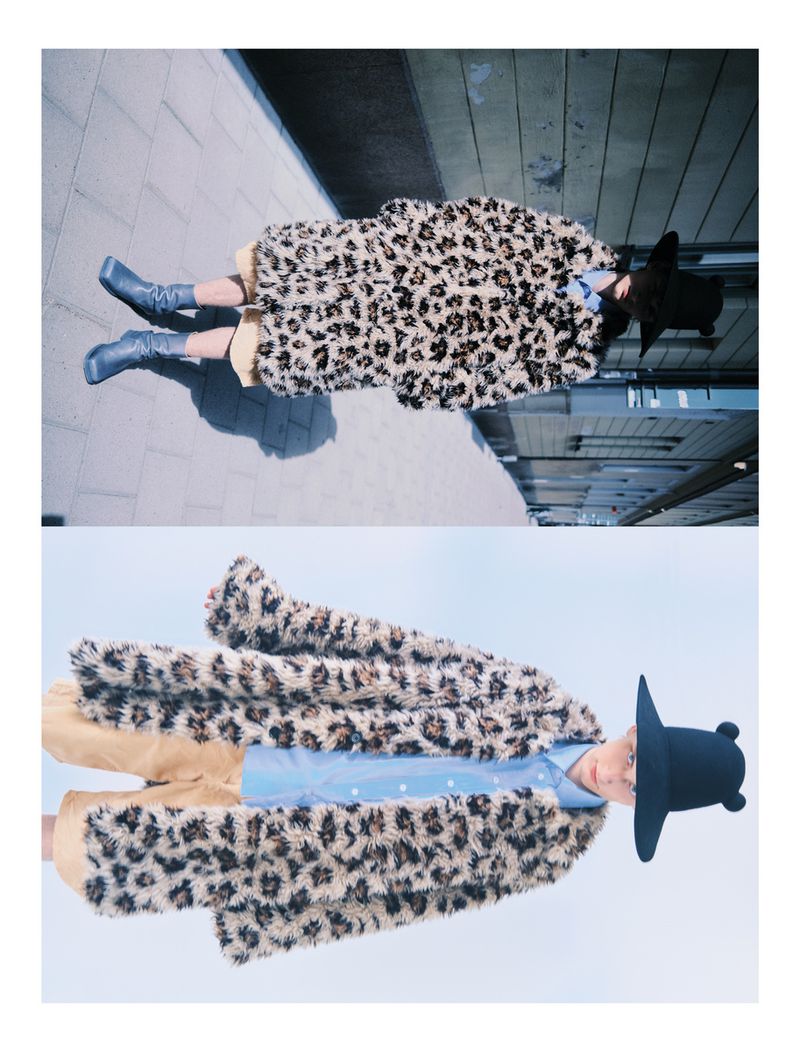 Fashionable person in an animal-print coat and hat, standing on concrete, mirrored in the lower half of the image for a surreal effect.