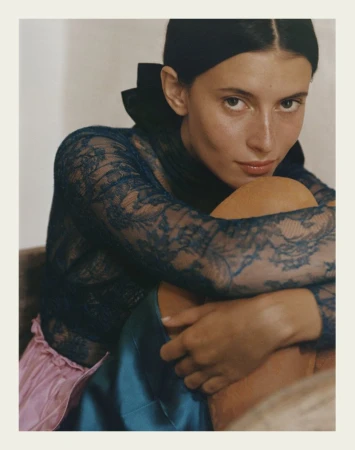 Portrait of a young woman in lace top with a black collar and silk skirt, indoors with a neutral background, eye-level angle.