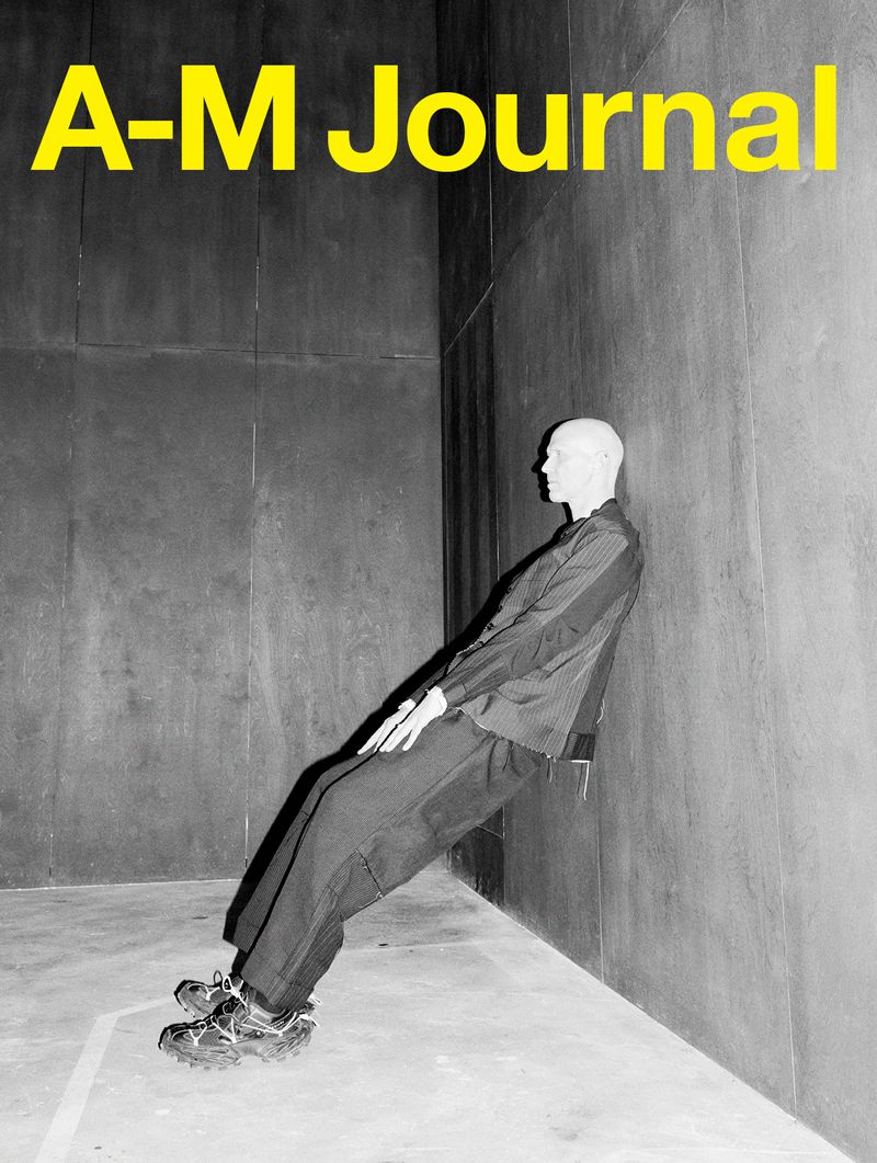 Monochrome portrait of an adult man leaning against a corner, set against a textured gray wall with bright yellow magazine text.