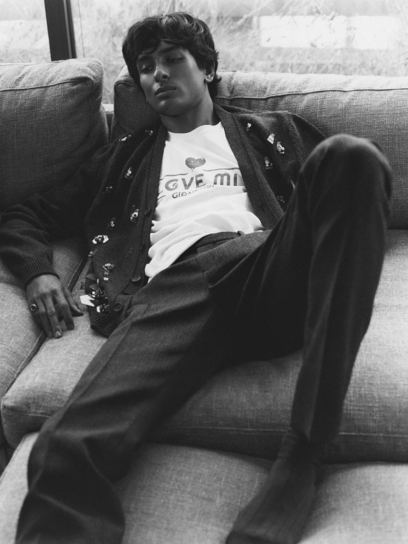 Monochrome portrait of a man wearing a cardigan and t-shirt, reclining on a couch, with natural light streaming through a window.