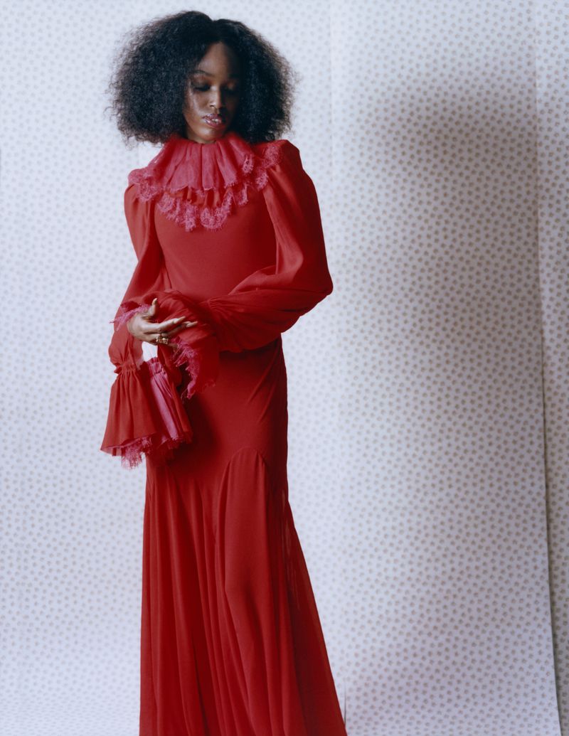 Elegant black woman in a ruffled red dress holding a matching bag, standing against a patterned backdrop, fashion photography.