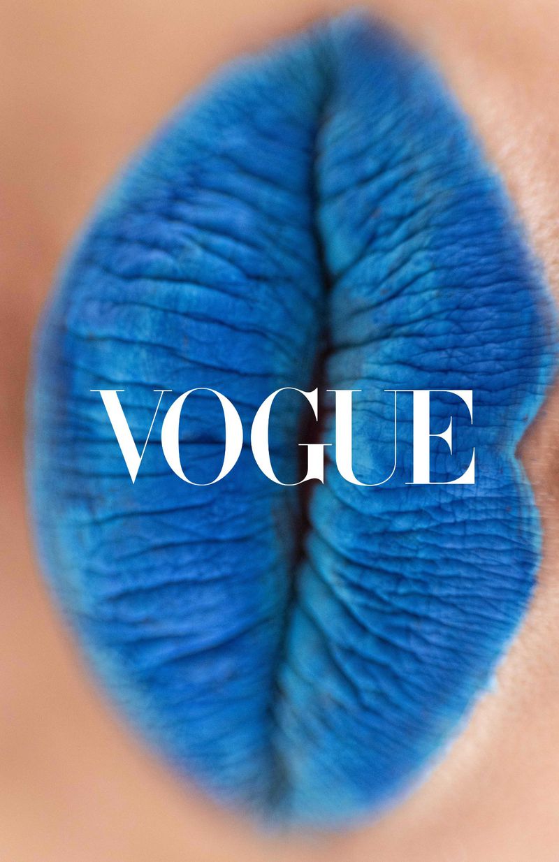 Close-up of lips painted bright blue with white "Vogue" text overlay, high-fashion, beauty, and cosmetic advertising campaign concept.