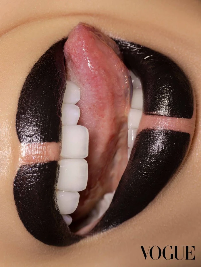 Macro close-up of open lips wearing graphic black lipstick with negative space stripes, showing teeth and tongue.