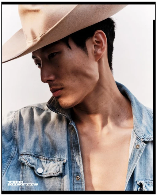 Portrait of an adult male model with tan cowboy hat and open denim shirt, medium shot in natural light, looking off-camera.