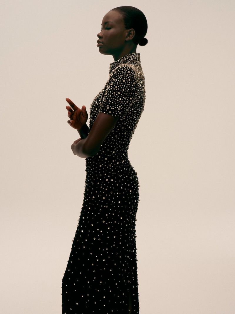 Elegant dark-skinned woman in a beaded evening gown, side profile against a bright background. Classy, formal wear fashion shot.