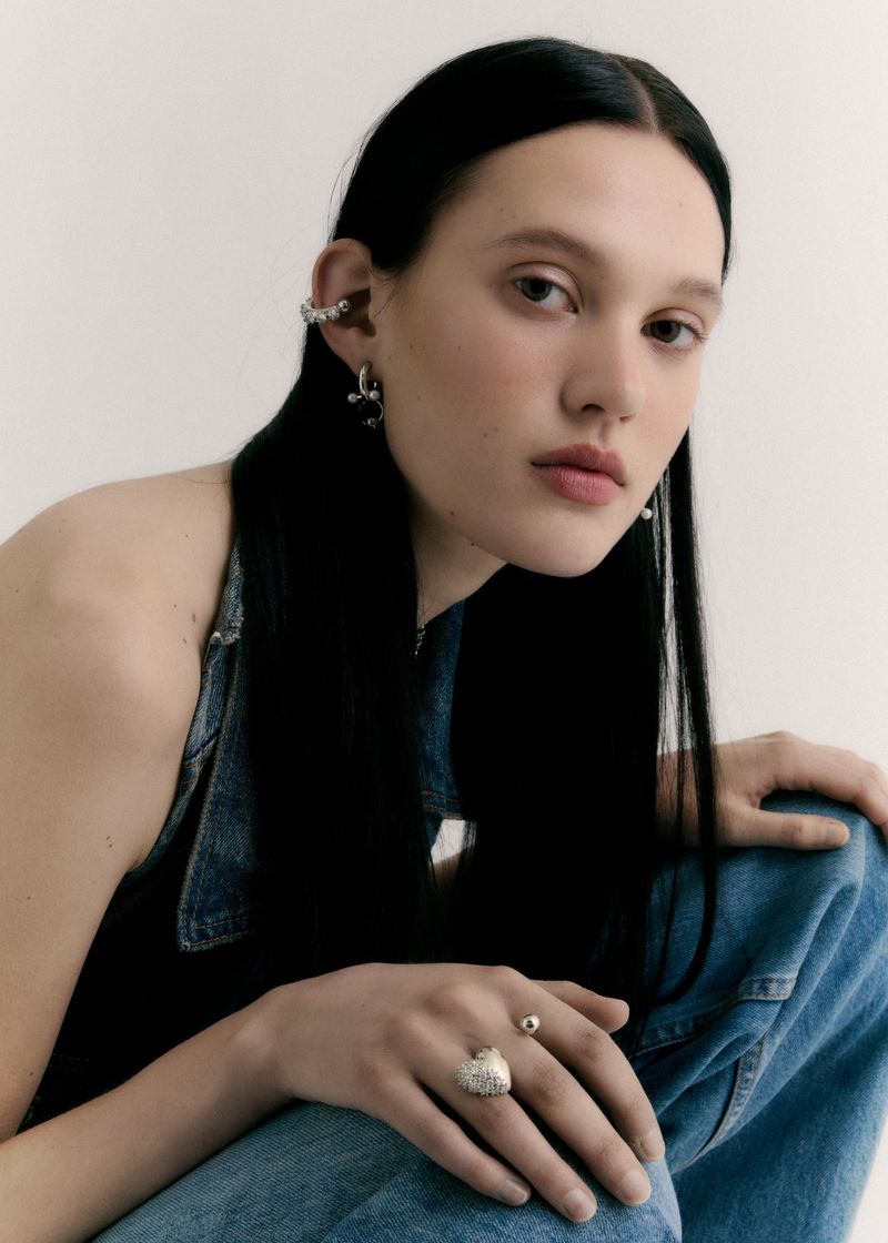 Close-up shot of a stylish woman wearing denim and jewelry against a neutral backdrop in a fashion editorial. Beauty and style.