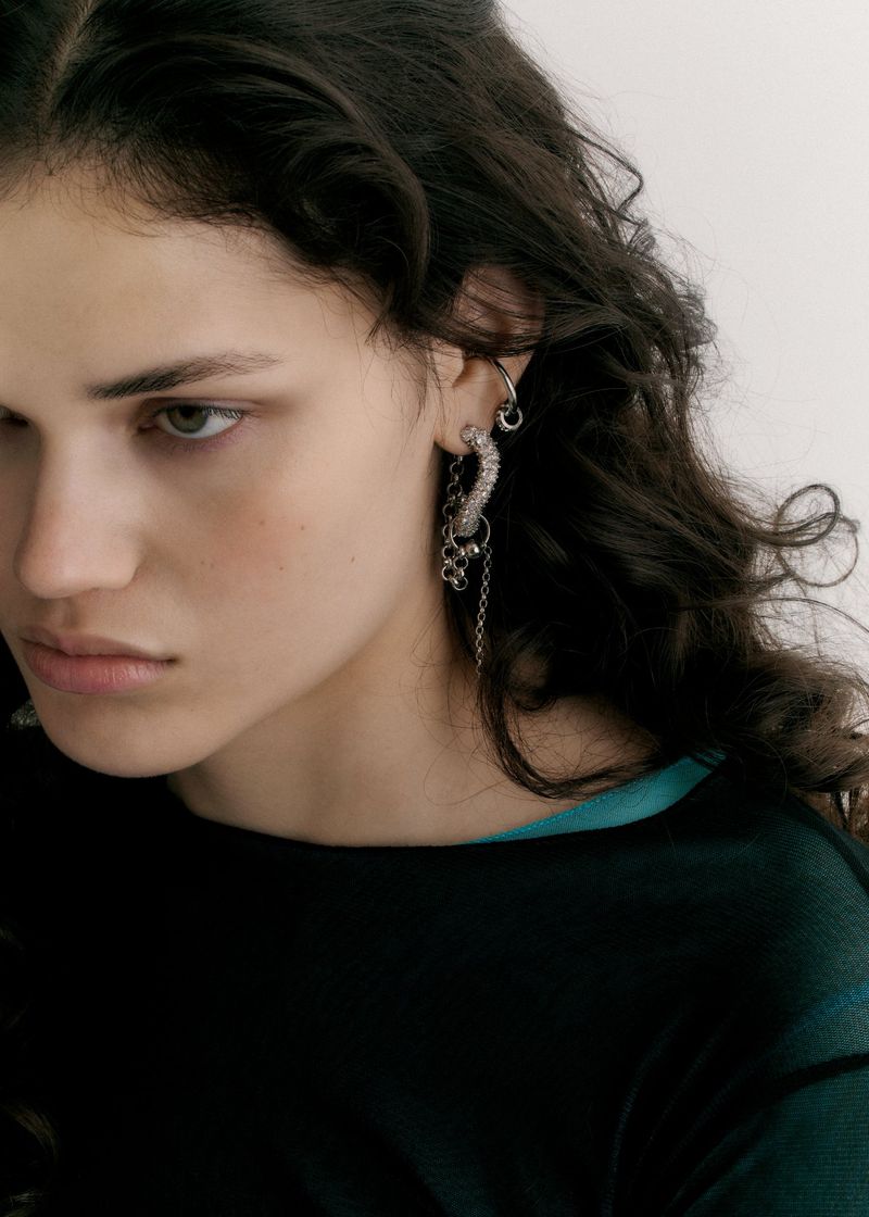 Close-up studio shot of a young adult woman wearing ornate silver jewelry, with dark wavy hair, against a plain white background.