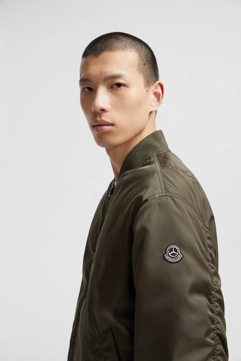 Close-up of a young Asian man in an olive green bomber jacket against a neutral background, showcasing minimalist fashion and style.