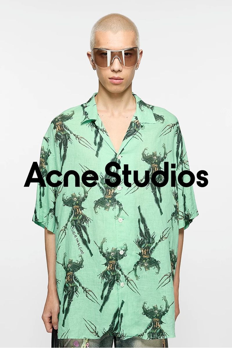 An adult male poses in front of a white backdrop, wearing oversized tinted glasses and a patterned short-sleeve shirt with 'Acne Studios' text overlay.