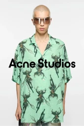 Model with shaved blonde hair wearing oversized green patterned shirt and futuristic sunglasses against white background