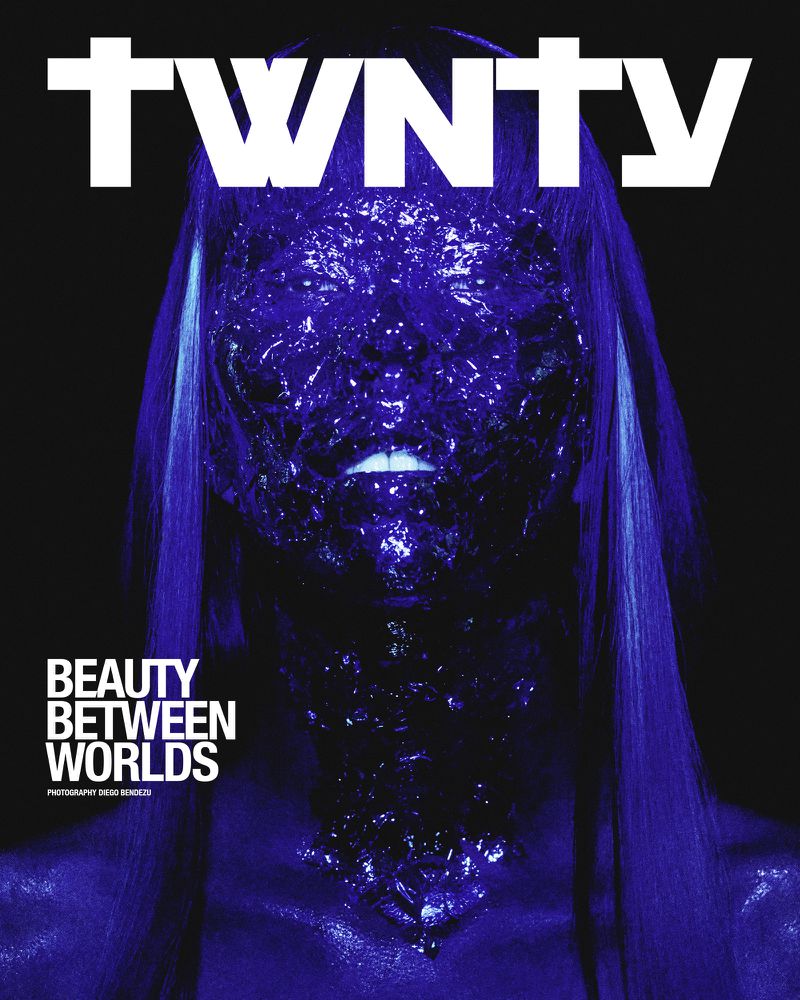 Magazine cover featuring a woman with blue hair and a shimmering blue face covered in glitter-like particles, against a dark backdrop.