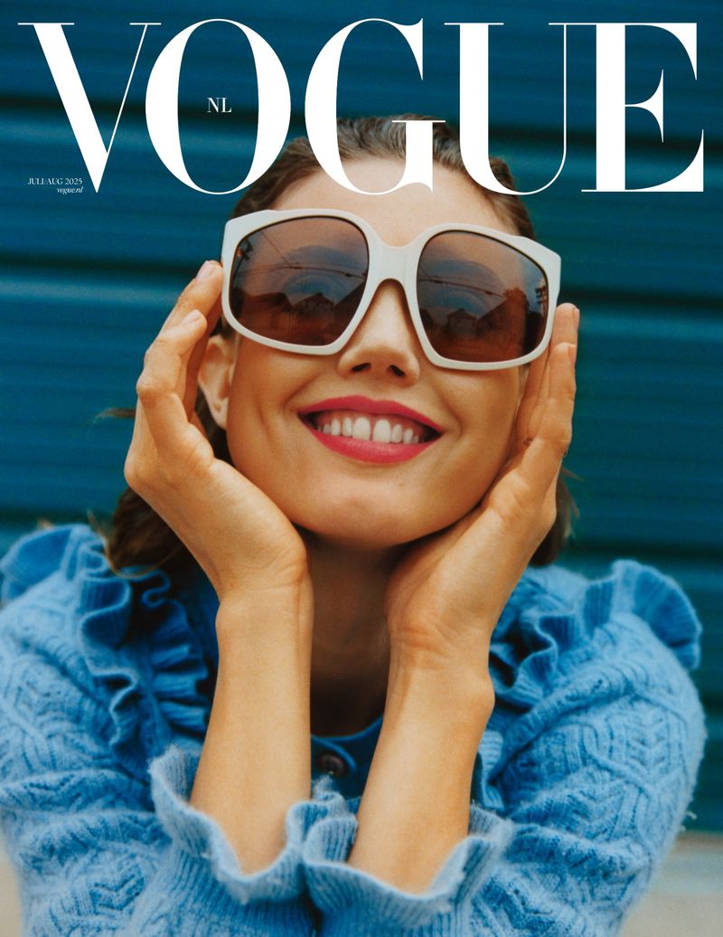 Vogue NL cover featuring a smiling woman with oversized sunglasses, a blue textured sweater, and a blue background.