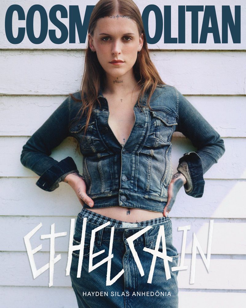 Ethel Cain poses in a denim jacket and jeans against a white wood wall for a magazine cover, with the magazine's title on top.